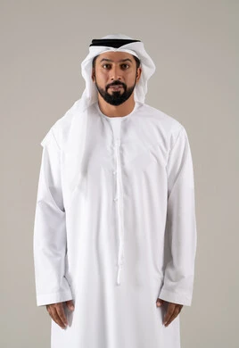 A personal photo for official documents, focusing on elegance and appearance, a portrait of an Emirati Gulf Arab man wearing a kandura and ghutrah, looking at the camera with gestures of self-confidence, with a gray background.