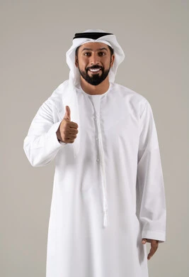 Gestures of quality, excellence, and distinction, expressing quality and craftsmanship, approval, satisfaction, and acceptance, a portrait of a young Arab Gulf Emirati man wearing a kandura and ghutrah, raising his thumb with gestures of joy, cheerfulness, and happiness, with a gray background.