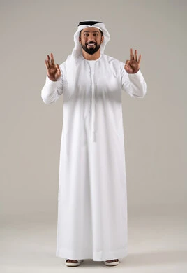 Standing with joy, cheerfulness, and happiness, expressing quality and craftsmanship, agreement, satisfaction, and acceptance, a portrait of a young Arab Gulf Emirati man wearing a kandura and ghutrah, raising his thumb with gestures of quality, excellence, and distinction, with a gray background.