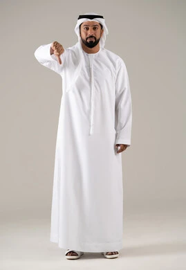 مفهوم الرفض وعدم القبول، بورترية لرجل عربي خليجي اماراتي يرتدي الكندورة والغترة يشير بإصبع الابهام للاسفل بإيماءات عدم الاعجاب والتقييم السلبي، الشعور بالانزعاج من شيء ما, خلفية رمادية