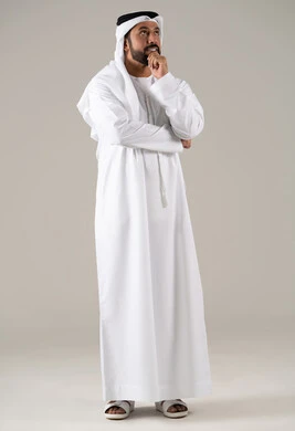 The concept of contemplation and focus, aspiration and planning for the future, problem-solving and decision-making, a portrait of an Arab Gulf Emirati man wearing a kandura and ghutrah, resting his hand on his chin with gestures of thinking and absent-mindedness, gray background.