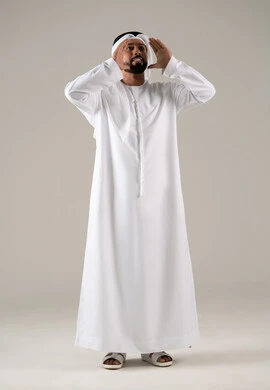 Calling and speaking loudly, a portrait of an Emirati Gulf Arab man wearing a kandura and ghutrah, placing his hand on his mouth in gestures of calling someone, chatting, conversations, and social communication, with a gray background.