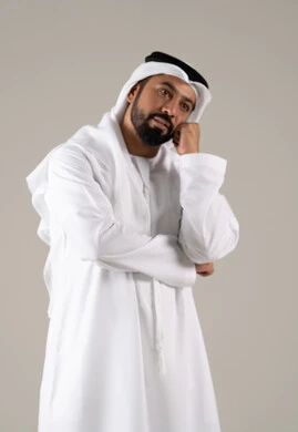 مفهوم القهر والخسارة، الندم والحسرة على شيء ما، بورتريه لرجل عربي خليجي اماراتي يرتدي الكندورة والغترة يضع يده على ذقنه بإيماءات الحزن، الشعور بالإنزعاج والخذلان، خلفية رمادية