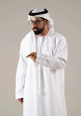The need for an eye examination, the concept of visual impairment, elegance and attention to appearance, a portrait of an Emirati Gulf Arab man wearing a kandura, ghutrah, and prescription glasses, with a gray background.