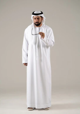 The necessity of needing a doctor, the need for an eye examination, the concept of visual impairment, elegance and attention to external appearance, a portrait of an Arab Gulf Emirati man wearing a kandura, ghutrah, and prescription glasses, with a gray background.
