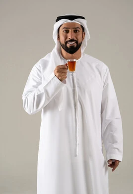 منتجات محلية وطنية اماراتيه ، بورتريه لرجل عربي خليجي اماراتي يرتدي الكندورة والغترة يحمل بيده كوب من الشاي، تعابير الجودة والامتياز ، الاستمتاع في تناول المشروبات الساخنه ، النظر بإيماءات السعادة ، مفهوم الاهتمام بالمظهر الخارجي،خلفية رمادية