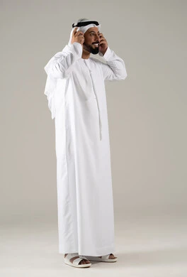 الاستماع الى الأغاني والموسيقى ، استخدام تقنية الهيدفون،بورتريه لرجل عربي خليجي اماراتي يرتدي الكندورة والغترة يضع سماعة الرأس يقوم بالإصغاء والاستماع إلى شيء ما، خلفية رمادية