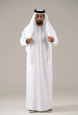 بورتريه لرجل عربي خليجي إماراتي يرتدي الكندورة ويعدل من وضعية الغترة البيضاء ينظر بتعابير السرور، الأناقة والاهتمام بالمظهر الخارجي، مفهوم الرجولة والثقة بالنفس,خلفية رماديه.