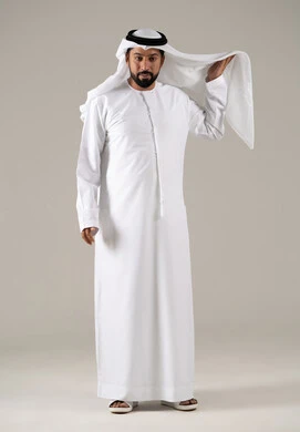 مفهوم الرجولة والثقة بالنفس, بورتريه لرجل عربي خليجي إماراتي يرتدي الكندورة ويعدل من وضعية الغترة البيضاء ينظر بتعابير السرور، الأناقة والاهتمام بالمظهر الخارجي، خلفية رماديه.
