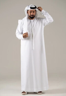 بورتريه لرجل عربي خليجي إماراتي يرتدي الكندورة ويعدل من وضعية الغترة البيضاء ينظر بتعابير السرور، الأناقة والاهتمام بالمظهر الخارجي، مفهوم الرجولة والثقة بالنفس,خلفية رماديه.