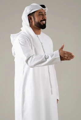 Gestures of joy and happiness, the concept of peace and welcome, facial expressions and different body language, a side portrait of an Emirati Gulf Arab man wearing a kandura and ghutrah extending his right hand to greet, gray background.
