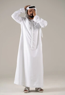 The feeling of migraine and headache, the sensation of fatigue and loss of concentration, stress and psychological pressure, a portrait of an Emirati Gulf Arab man wearing a kandura and ghutrah, placing his hands on his head and closing his eyes with gestures of severe head pain, gray background.
