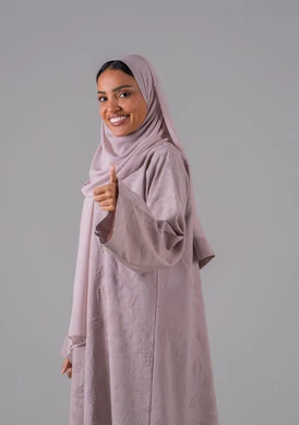 A portrait of a Saudi Arabian Gulf woman wearing an abaya and hijab, gesturing with her hand and showing facial expressions and hand movements that indicate admiration, expression of mastery, acceptance, agreement, and satisfaction, a sign of quality and excellence, with a gray background.