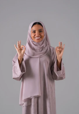 بورتريه لامراه عربيه خليجيه سعودية ترتدي العباءة والحجاب تشير بيدها بإيماءات وتعابير وجه و يدين تدل على الاعجاب، التعبير عن الاتقان، القبول والموافقة والرضا، علامة الجودة والامتياز،خلفية رمادية