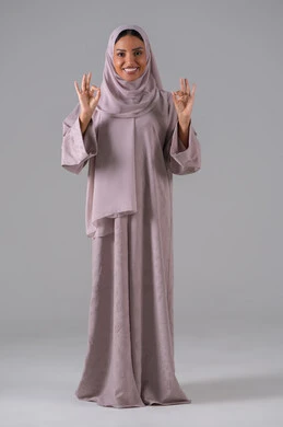 علامة الجودة والامتياز، بورتريه لامراه عربيه خليجيه سعودية ترتدي العباءة والحجاب تشير بيدها بإيماءات وتعابير وجه و يدين تدل على الاعجاب، التعبير عن الاتقان، القبول والموافقة والرضا، خلفية رمادية