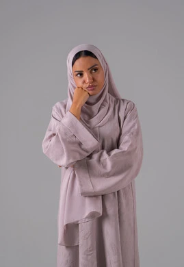 مفهوم القهر والخسارة، الندم والحسرة على شيء ما، بورتريه لامراه عربيه خليجيه سعودية ترتدي العباءة والحجاب تضع يدها على ذقنها بإيماءات الحزن، الشعور بالإنزعاج والخذلان، خلفية رمادية