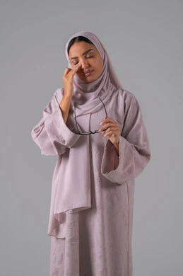 Elegance and attention to appearance, the concept of visual impairment, a portrait of a Saudi Arabian Gulf woman wearing an abaya, hijab, and prescription glasses with gestures of interaction and integration, gray background.