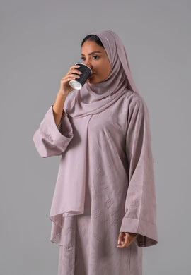 النظر بإيماءات الاندماج ، الاستمتاع في تناول المشروبات الساخنه ،مفهوم الاهتمام بالمظهر الخارجي، منتجات محلية وطنية سعودية، بورتريه لامراة عربيه خليجية سعودية ترتدي العباءة والحجاب تحمل بيدها كوب من القهوة، خلفية رمادية