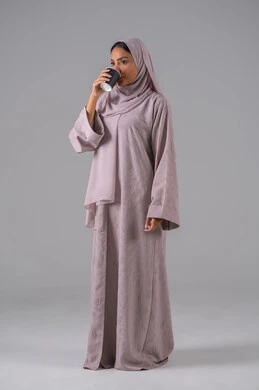 الاستمتاع في تناول المشروبات الساخنه ، النظر بإيماءات الاندماج ، مفهوم الاهتمام بالمظهر الخارجي، منتجات محلية وطنية سعودية، بورتريه لامراة عربيه خليجية سعودية ترتدي العباءة والحجاب تحمل بيدها كوب من القهوة، خلفية رمادية