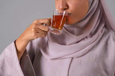 تعابير الجودة والامتياز ، الاستمتاع في تناول المشروبات الساخنه ، النظر بإيماءات السعادة ، مفهوم الاهتمام بالمظهر الخارجي، منتجات محلية وطنية سعودية، بورتريه لامراة عربيه خليجية سعودية ترتدي العباءة والحجاب تحمل بيدها كوب من الشاي، خلفية رمادية