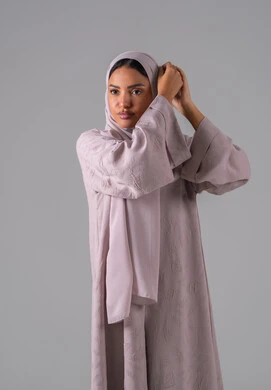 مفهوم الأنوثة والنعومة, الاهتمام بالأناقة والمظهر الخارجي, أزياء محجبات عصرية أنيقة, بورترية لشابة عربية خليجية سعودية ترتدي العباءة وتعدل من وضعية الحجاب تقف بتعابير الثقة والاعتزاز بالنفس ، خلفية رمادية