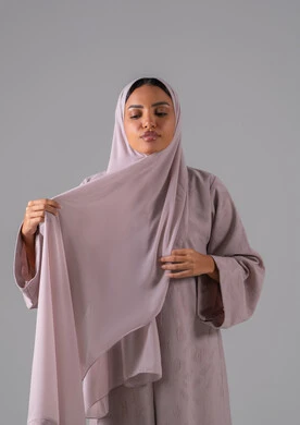 تعابير الثقة والاعتزاز بالنفس، الاهتمام بالأناقة والمظهر الخارجي, مفهوم الأنوثة والنعومة, أزياء محجبات عصرية أنيقة, بورترية لشابة عربية خليجية سعودية ترتدي العباءة وتعدل من وضعية الحجاب، خلفية رمادية