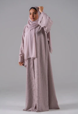 The concept of femininity and softness, the interest in elegance and appearance, modern elegant hijab fashion, a portrait of a young Arab Gulf Saudi woman wearing an abaya and adjusting her hijab, standing with expressions of confidence and self-pride, with a gray background.