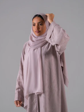 الاهتمام بالأناقة والمظهر الخارجي, مفهوم الأنوثة والنعومة, أزياء محجبات عصرية أنيقة, بورترية لشابة عربية خليجية سعودية ترتدي العباءة وتعدل من وضعية الحجاب تقف بتعابير الثقة والاعتزاز بالنفس ، خلفية رمادية