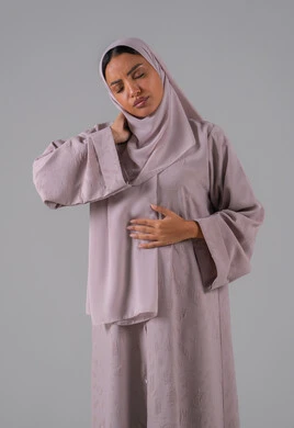 Neck, bone, and spine pain, gestures of distress and suffering, a portrait of a Gulf Arab Saudi woman wearing an abaya and hijab holding her neck with gestures of pain, the necessity to see a doctor and receive treatment, gray background.