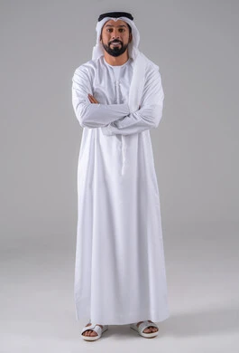 مفهوم الرجولة والثقة بالنفس, الوقوف باستقامة وايدي متقاطعة، بورتريه لرجل عربي خليجي إماراتي يرتدي الكندورة والغترة البيضاء ينظر بتعابير السرور، الأناقة والاهتمام بالمظهر الخارجي، خلفية رماديه.