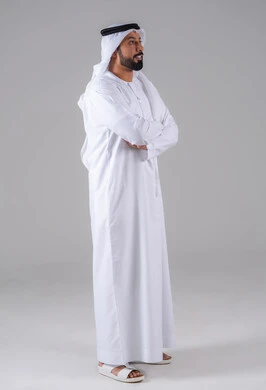 الأناقة والاهتمام بالمظهر الخارجي، الوقوف باستقامة وايدي متقاطعة، مفهوم الرجولة والثقة بالنفس, بورتريه من الجانب لرجل عربي خليجي إماراتي يرتدي الكندورة والغترة البيضاء ينظر بتعابير السرور، خلفية رماديه.