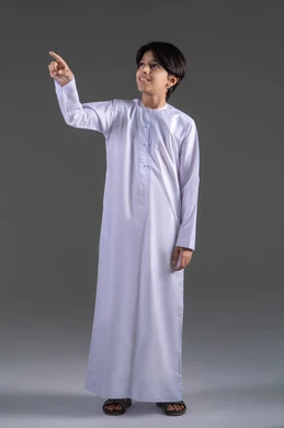 الاشارة الى مكان ما بواسطة اصبع السبابة, بورتريه  لولد عربي خليجي سعودي يرتدي الثوب الابيض التقليدي يشير باصبعه لشيء ما بايماءات السعادة, تحديد موقع والاشارة اليه, اشارات وحركات معبرة،الاناقة والاهتمام بالمظهر الخارجي، الجسم بالطول الكامل, خلفية رمادي