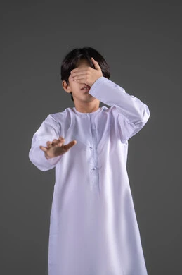 محاولةالوصول و  التركيز على شيء ما، الم في العيون والرأس ، عدم وضوح الرؤية بشكل جيد، إغلاق العيون باستخدم اليدين، بورتريه لولدعربي خليجي سعودي يرتدي الثوب التقليدي  يضع يده على عينيه بشكل  بإيماءات عدم العثور على شيء، الجسم بالطول الكامل، خلفية رمادي