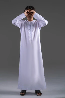 التخطيط للأهداف والطموحات المستقبلية، محاولة تقريب الأشياء البعيدة،  حب الاكتشاف والمعرفة والمغامرة، التركيز على شيء ما، بورتريه لولدعربي خليجي سعودي يرتدي الثوب التقليدي  يضع يده على عينيه بشكل عدسة بإيماءات البحث، الجسم بالطول الكامل، خلفية رمادي