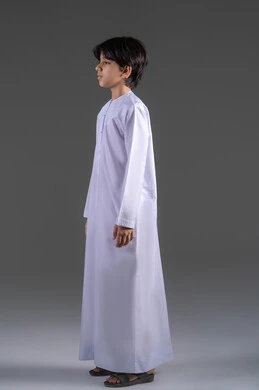 ملامح الوسامة والرجولة منذ الصغر,  التجهز والاستعداد  للذهاب للخارج، الاهتمام في المظهر الخارجي، النظر الى الكاميرا بايماءات السعادة و السرور، بورترية من الجانب لولد عربي خليجي سعودي يرتدي الثوب التقليدي الابيض , الجسم بالطول الكامل ، خلفية رمادي