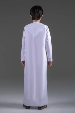 الاستعداد والتجهز للذهاب للخارج،  الاهتمام في المظهر الخارجي، النظر الى الكاميرا بايماءات السعادة و السرور، بورترية من الخلف لولد عربي خليجي سعودي يرتدي الثوب التقليدي الابيض , ايماءات الوسامة والرجولة منذ الصغر, الجسم بالطول الكامل ، خلفية رمادي