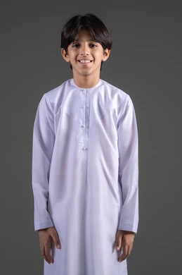 الاهتمام في المظهر الخارجي، النظر الى الكاميرا بايماءات السعادة و السرور، بورترية لولد عربي خليجي سعودي يرتدي الثوب التقليدي الابيض , الاستعداد والتجهز للذهاب للخارج، ايماءات الوسامة والرجولة منذ الصغر, الجسم بالطول الكامل ، خلفية رمادي