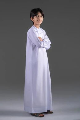 النظر الى الكاميرابتعابير السرور والسعادة, بورتريه لفتى عربي خليجي سعودي يرتدي الثوب الابيض التقليدي يقف بايدي متقاطعة, مفهوم الاناقة والهتمام بالمظهر الخارجي، مفهوم الثقه بالنفس،  التقاط صور شخصية للوثائق الرسمية،الجسم بالطول الكامل, خلفية رمادي