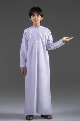 He opens his hands to display something, presenting something with his indicated hands, standing upright and straight, pointing to the palm of his hand, presenting and showcasing an item, lifting and carrying items, a portrait of an Arab Gulf Saudi boy wearing a traditional white thobe looking at the camera raising his hand forward with gestures of holding something, gray background.