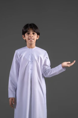 يعرض شيء بيديه المشار إليها , الوقوف باستقامة واعتدال, الإشارة إلى كف اليد,  تقديم وعرض عنصر ما، رفع وحمل العناصر،  بورتريه لولد عربي خليجي سعودي يرتدي الثوب التقليدي الابيض ينظر الى الكاميرا يرفع يده الى الأمام بايماءات حمل شيء، خلفية رمادي