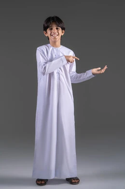 Standing upright and straight, pointing to the palm of the hand, presenting and displaying an item, lifting and carrying items, using the sense of touch to move holographic elements, a portrait of a Saudi Arabian Gulf boy wearing a traditional white thobe looking at the camera raising his hand forward with gestures of carrying something, gray background.
