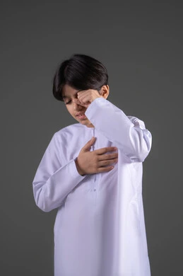 البكاء ومشاعر الحزن، إغماض العينين وعدم الرغبة بالرؤية، الشعور بالخجل والإحراج، التعرض لصدمة وعدم التصديق، بورتريه لولد عربي خليجي سعودي يرتدي الثوب التقليدي يغطي وجهه بيديه، الجسم بالطول الكامل، المشاعر والاحاسيس المرهفة، خلفية رمادي