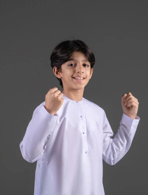 الانتصار والفوز والنجاح، مفهوم الانجاز وتحقيق الاهداف، بورتريه لفتى عربي خليجي سعودي مبتسم يرتدي الثوب الابيض التقليدي يرفع قبضتي يديه للاعلى بإيماءات الفرح والسرور, التشجيع بتعابير الحماس، زيادة قدرة العضلات على التحمل، الشعور بالسعادة والقوة، خلفية رمادي