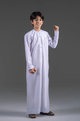 التشجيع بتعابير الحماس، زيادة قدرة العضلات على التحمل، الانتصار والفوز والنجاح، مفهوم الانجاز وتحقيق الاهداف، بورتريه لفتى عربي خليجي سعودي مبتسم يرتدي الثوب الابيض التقليدي يرفع قبضة يده للاعلى بإيماءات الفرح والسرور, الشعور بالسعادة والقوة، خلفية رمادي