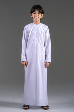 مفهوم الاهتمام في المظهر الخارجي، النظر الى الكاميرا بايماءات السعادة و السرور، بورترية لولد عربي خليجي سعودي يرتدي الثوب التقليدي الابيض , الاستعداد والتجهز للذهاب للخارج، ايماءات الوسامة والرجولة, الجسم بالطول الكامل ، خلفية رمادي