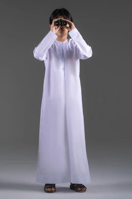 رؤية الاشياء البعيدة عبر المنظار،  تعابير التركيز والتفاعل، التخطيط المستقبلي للأهداف والطموحات، بورتريه لولد عربي خليجي سعودي مبتسم يرتدي الثوب التقليدي يحمل بيده المنظار ثنائي العينين، حب الاستكشاف والمغامرة، الجسم بالطول الكامل، خلفية رمادية