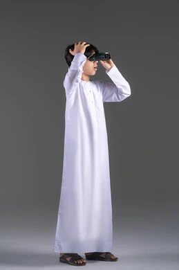 Love for adventure and exploration, seeing distant things through a telescope, a portrait of an Emirati Gulf Arab boy wearing a kandura looking through a binocular (telescope) with gestures of joy and happiness, future planning for goals and ambitions, full-body image, gray background.