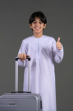 Thumbs up with gestures of admiration, a portrait of an Emirati Gulf Arab boy wearing a kandura holding a travel bag, enjoying a fun recreational trip, wellness and travel trips, gray background. Thumbs up with gestures of admiration, a portrait of an Emirati Gulf Arab boy wearing a kandura holding a travel bag, enjoying a fun recreational trip, wellness and travel trips, gray background.