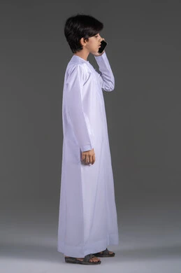 التواصل والدردشة مع الأصدقاء والاقارب، بورتريه لشاب عربي خليجي اماراتي  يرتدي الثوب التقليدي يقوم بإجراء مكالمة هاتفية عبر الجوال، قضاء وقت ممتع بتبادل الأحاديث، خلفية رمادية