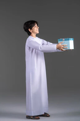 التعبير عن الألفة والمحبة, تقديم الهدايا في الأعياد والمناسبات,  بورتريه لولدعربي خليجي اماراتي مبتسم يرتدي الثوب التقليدي يحمل علبة هدية زرقاء ,صورة جانبية ، خلفية رمادية